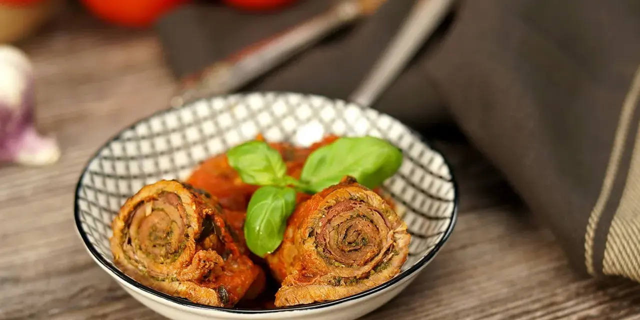 Zwei herzhafte involtini originalrezept in Tomatensoße, garniert mit Basilikum, in einer Schale auf Holztisch.