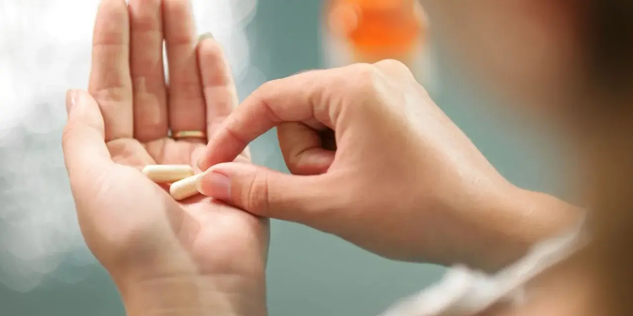 Dłoń trzyma kapsułki, które mogą być lekami do hormonalnej terapii zastępczej.