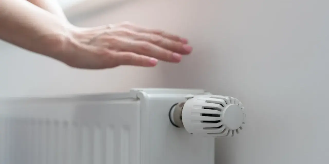 Dłoń nad grzejnikiem, sprawdzająca ciepło. Rozpoczyna się sezon grzewczy, czas na komfortowe ogrzewanie.