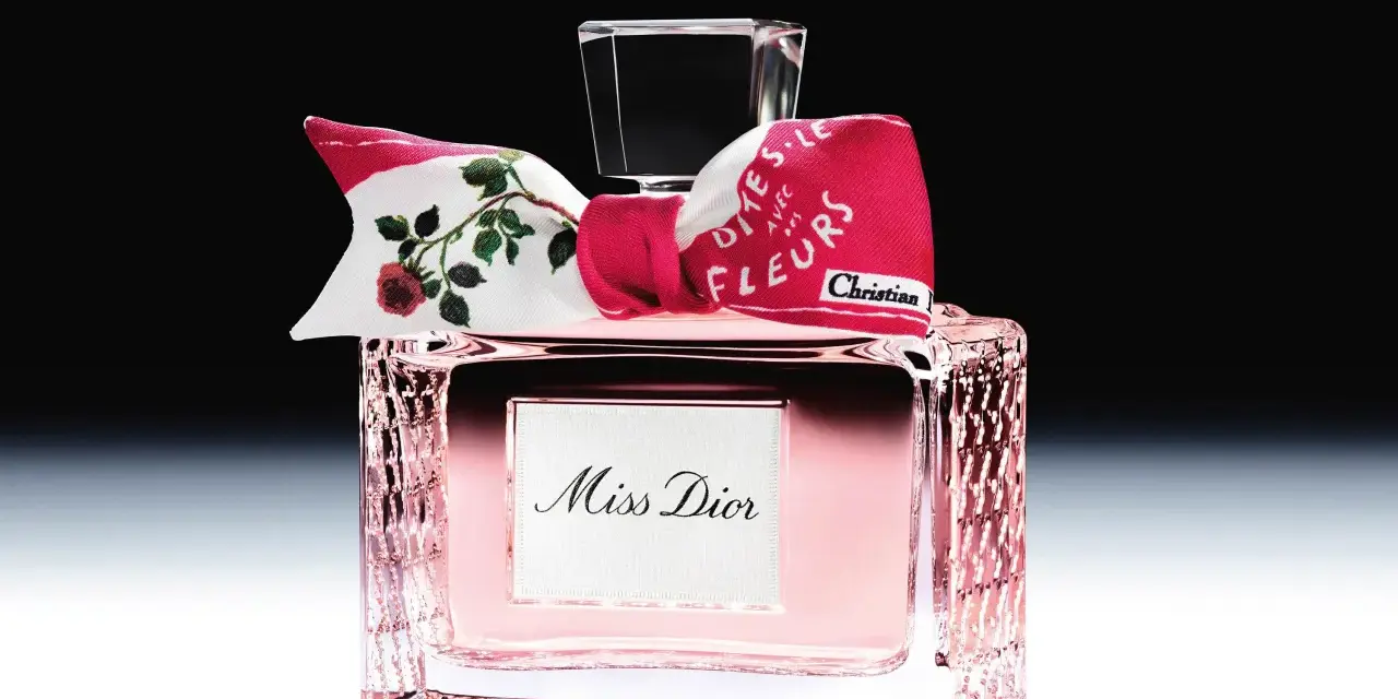 Eleganckie perfumy Miss Dior w różowym flakonie, ozdobione kokardką z motywem róż i napisem "Dites-le avec des fleurs".