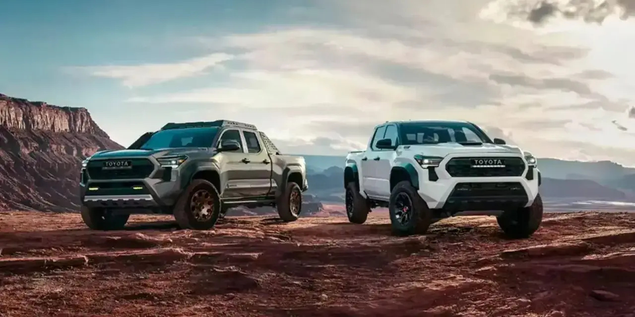 Dwa nowe modele toyota pickup, biały i szary, gotowe na przygodę w surowym, pustynnym krajobrazie.