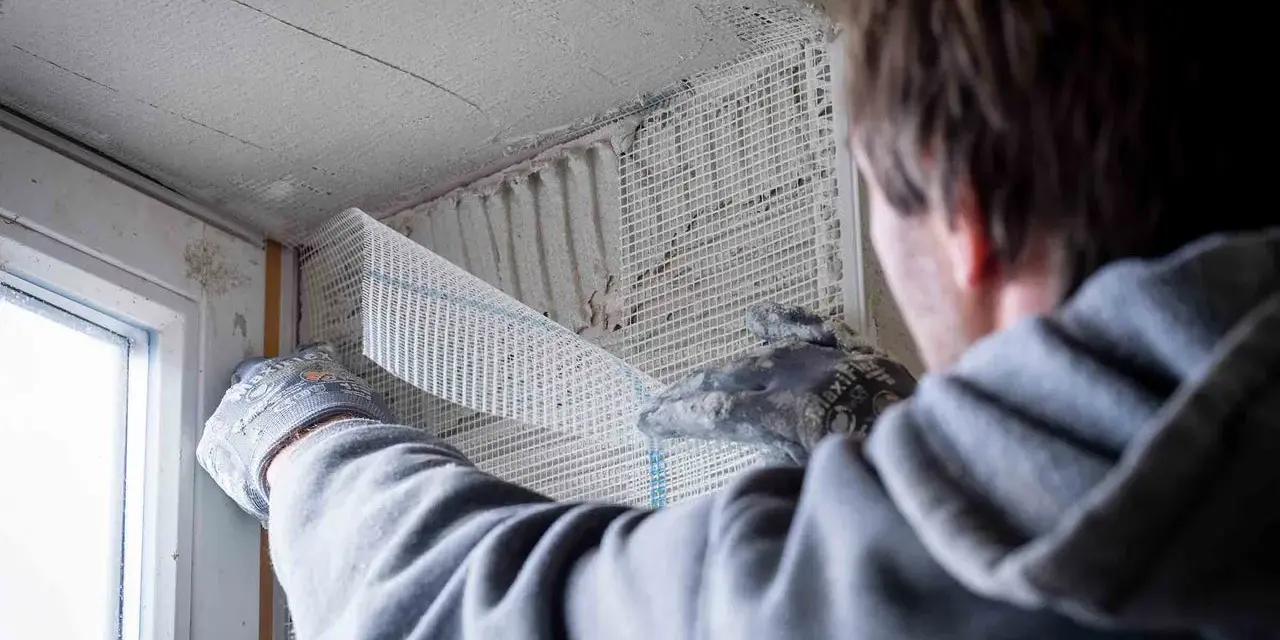 Hand mit Handschuh legt Armierungsgewebe an, um die Fensterlaibung zu verputzen.