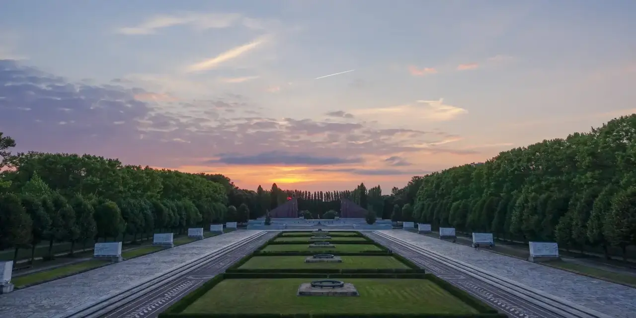 Sonnenuntergang über dem Sowjetischen Ehrenmal in Berlin. Ein beeindruckendes Beispiel für Parks in Berlin, mit symmetrischen Rasenflächen und einer langen Allee.