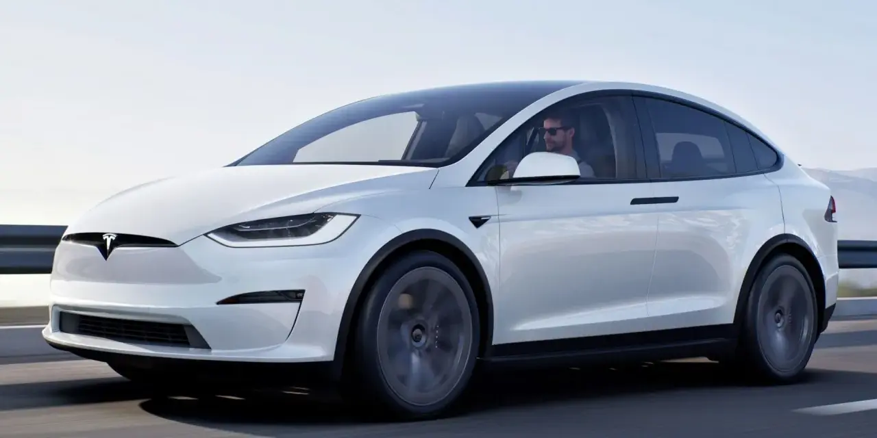 Biały Tesla X w ruchu, kierowca w okularach. Zastanawiasz się nad jego ceną?