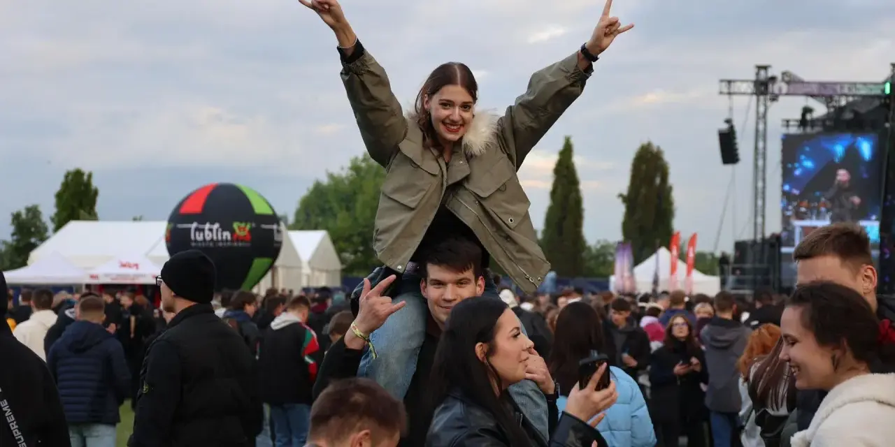 Dziewczyna na ramionach chłopaka cieszy się na Juwenaliach Politechniki Lubelskiej. W tle scena i tłum bawiących się studentów.