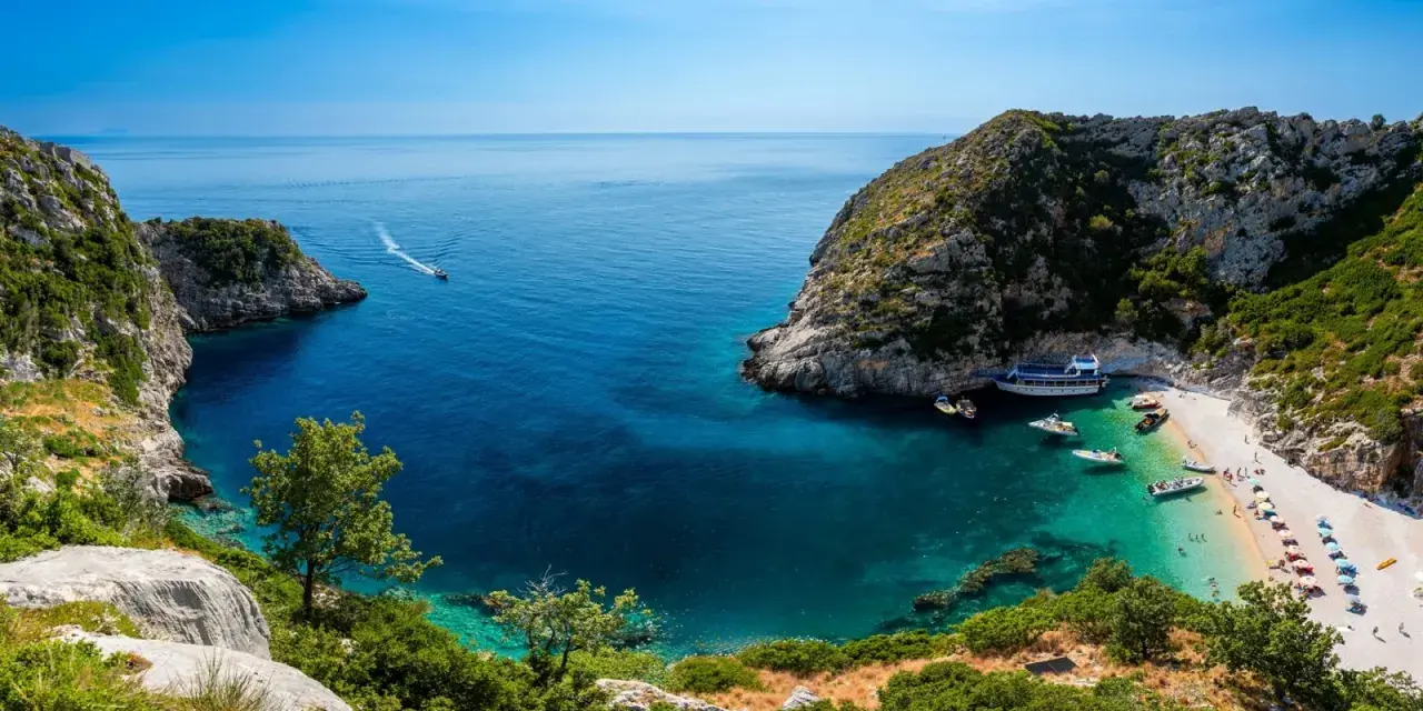 Malownicza zatoka z krystalicznie czystą wodą, plażą i łodziami. Idealne miejsce na wczasy samolotem all inclusive w Albanii.