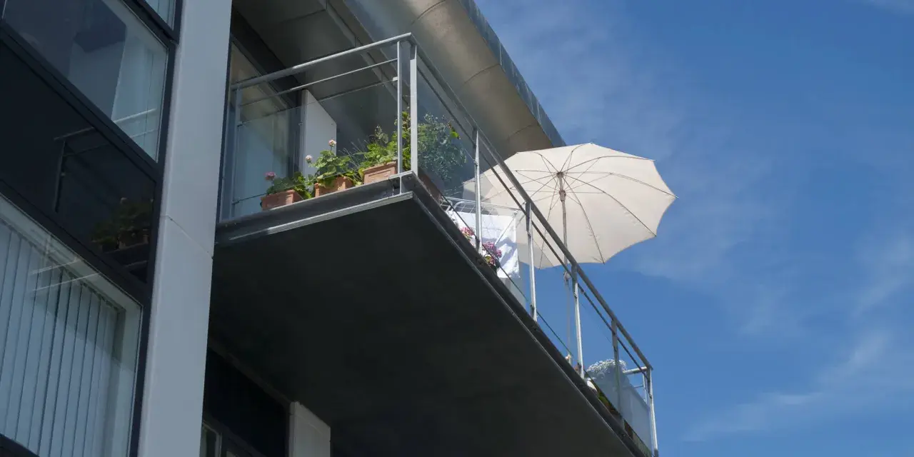 Balcon en béton moderne, prêt pour une rénovation. Des plantes en pot et un parasol blanc attendent le soleil.
