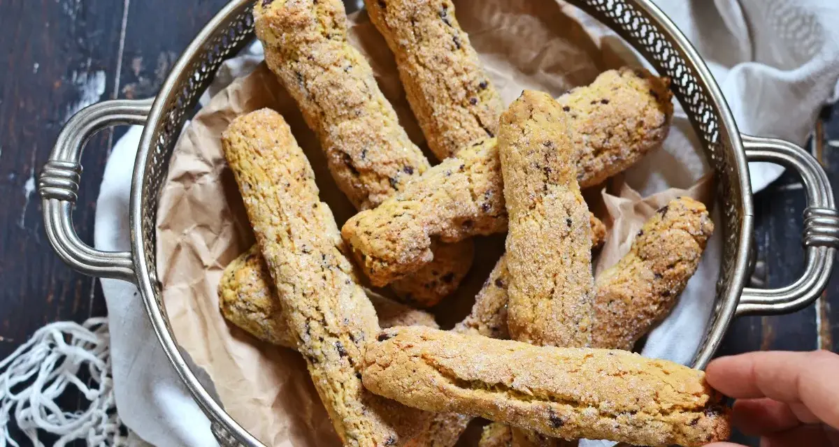 Biscotti senza farina dorati e croccanti, cosparsi di zucchero, in un cestino d'argento. Una mano ne prende uno.