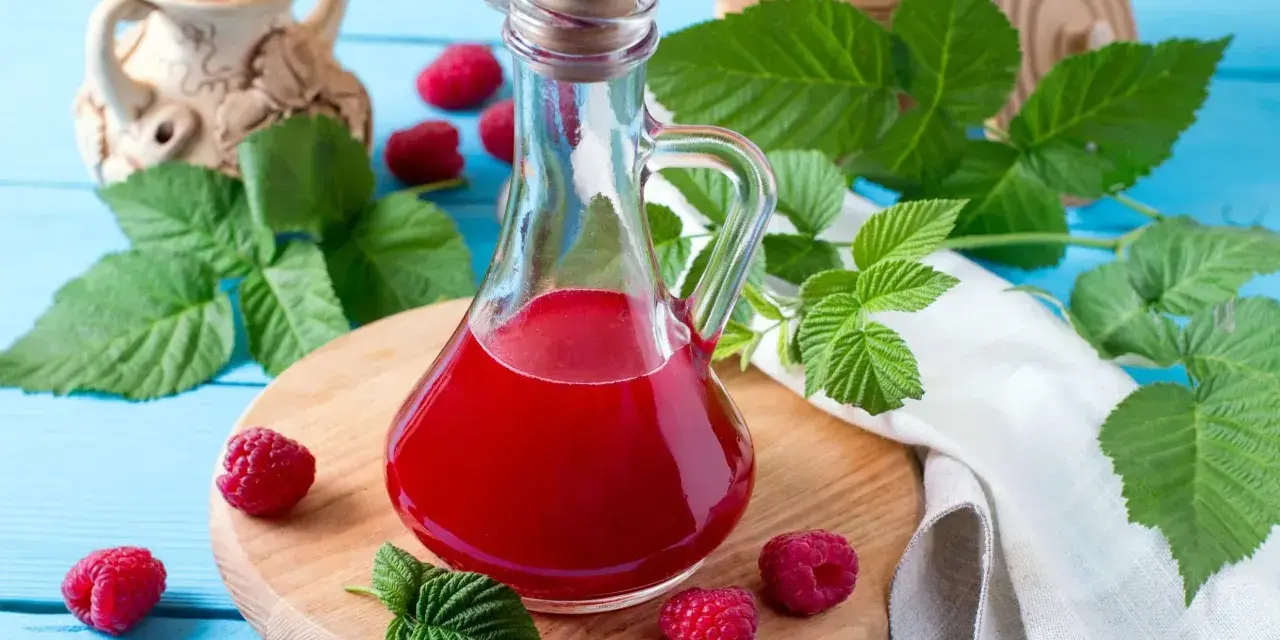 Malinowy ocet balsamiczny do sałatek, deserów, marynat. W butelce z korkiem, otoczony świeżymi malinami i liśćmi.