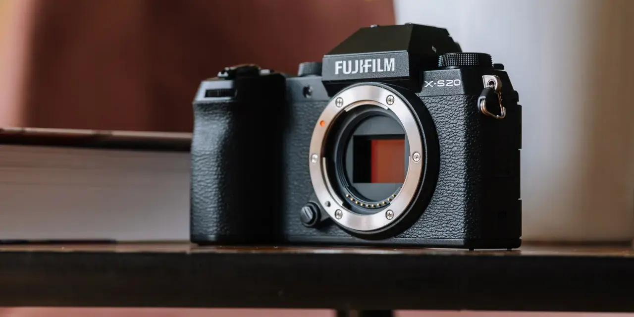 Czarny aparat Fujifilm X-S20 z obiektywem bez obiektywu, leżący na drewnianym stole obok książki.