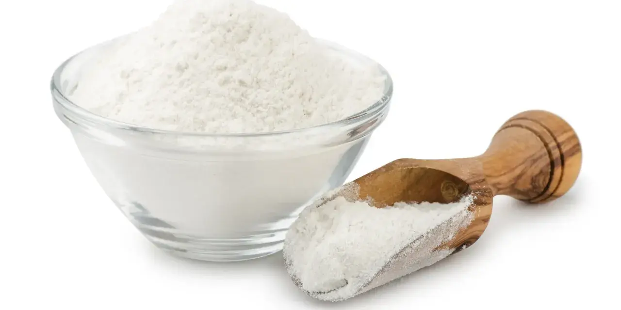 Una ciotola di vetro piena di polvere bianca, probabilmente aluminum starch octenylsuccinate, e un cucchiaio di legno con la stessa polvere.