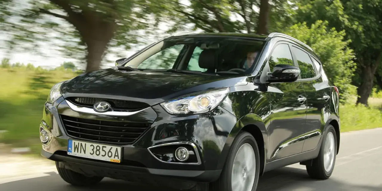 Czarny Hyundai ix35 jedzie drogą wśród zieleni.