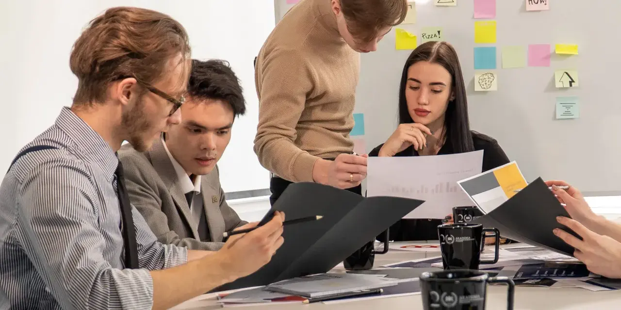 Studenci analizują wykresy, przygotowując się do zajęć z handlu międzynarodowego. Na tablicy notatki i pomysły.
