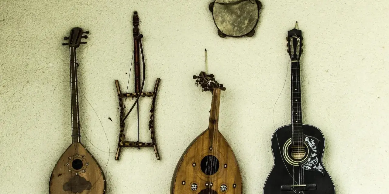 Verschiedene Saiteninstrumente und ein Tamburin hängen an der Wand. Seit wann gibt es Gitarren? Die Geschichte der Gitarre reicht weit zurück.