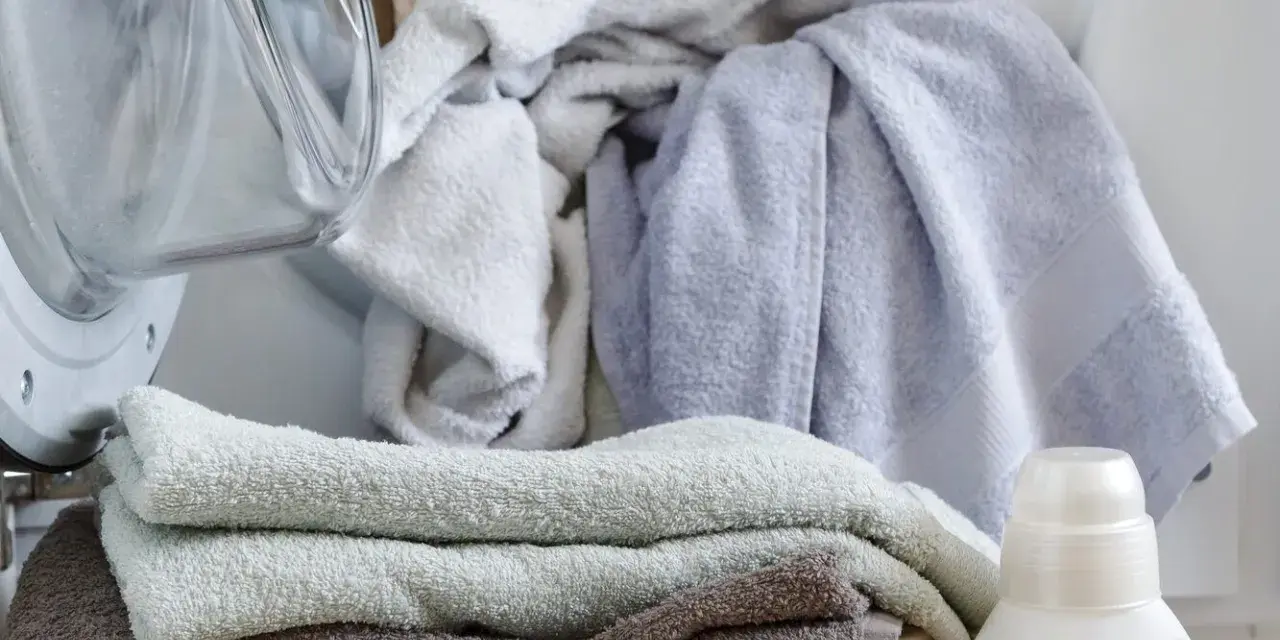 Pranie delikatnych ręczników dla dzieci. Obok pralki kosz z czystymi ręcznikami i butelka płynu do prania dla dzieci.