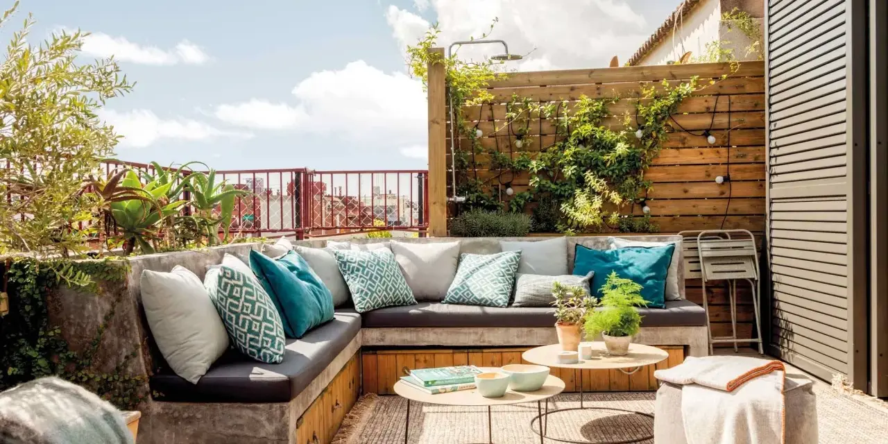 Cómodo rincón de terraza con sofás de obra, cojines turquesas y plantas. Ideas para jardineras exteriores que inspiran relax.