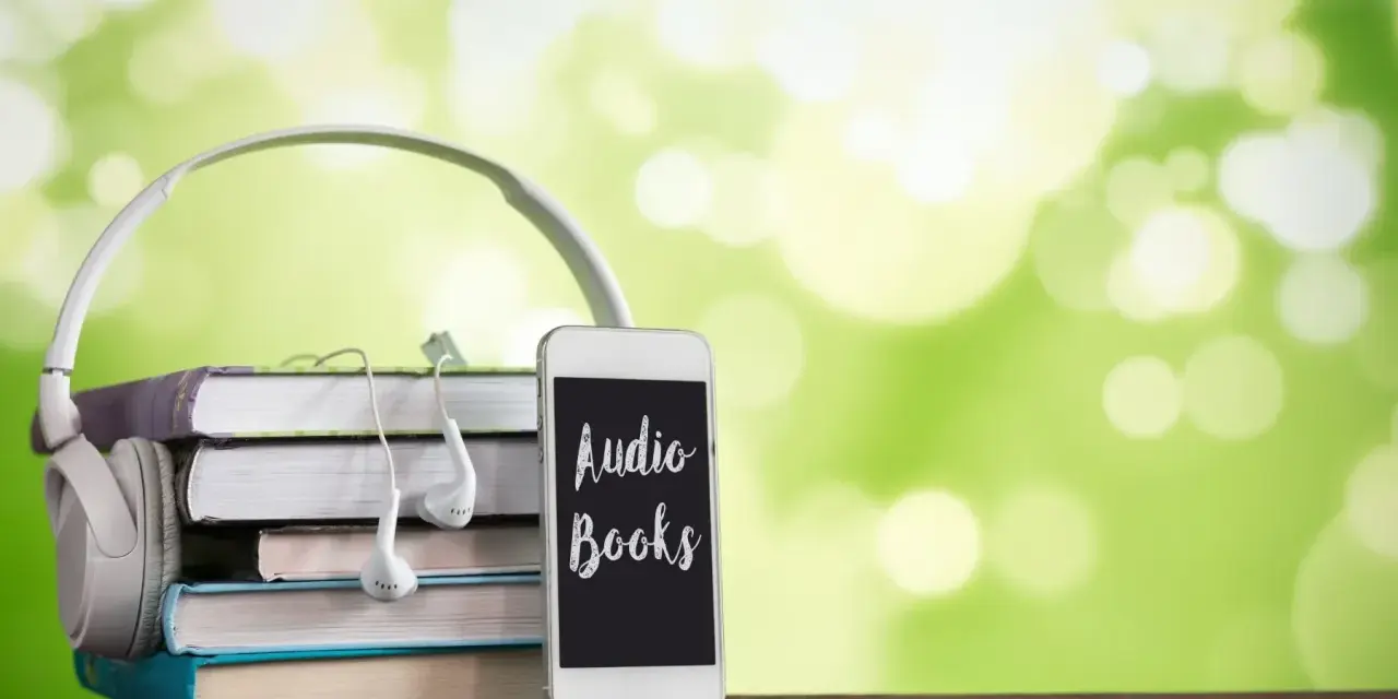 Słuchawki, stos książek i telefon z napisem "Audio Books" – idealne połączenie do odkrywania najpiękniejszych słuchowisk dla dzieci.