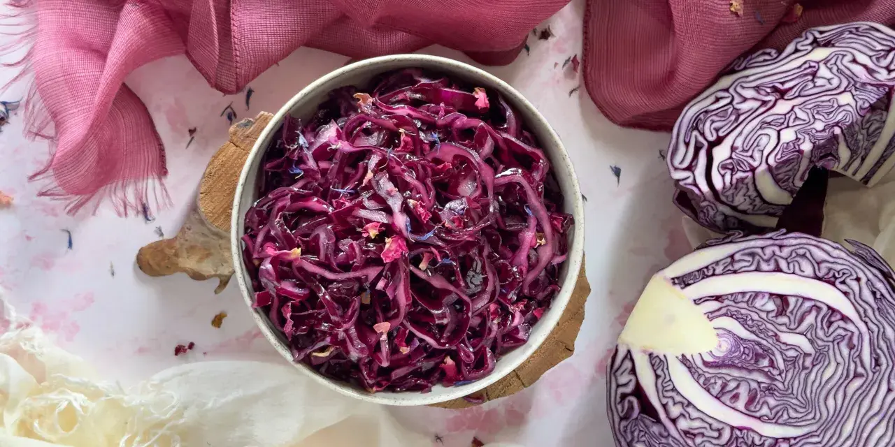 Insalata di cavolo cappuccio rosso, condita con petali di fiori, accanto a un cavolo cappuccio rosso tagliato a metà.