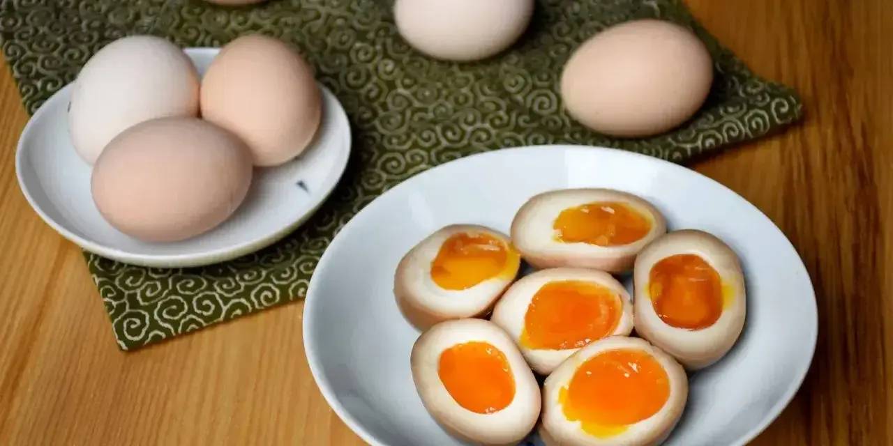 Na talerzu leżą połówki jajek do ramenu z płynnym, pomarańczowym żółtkiem. Obok całe jajka.