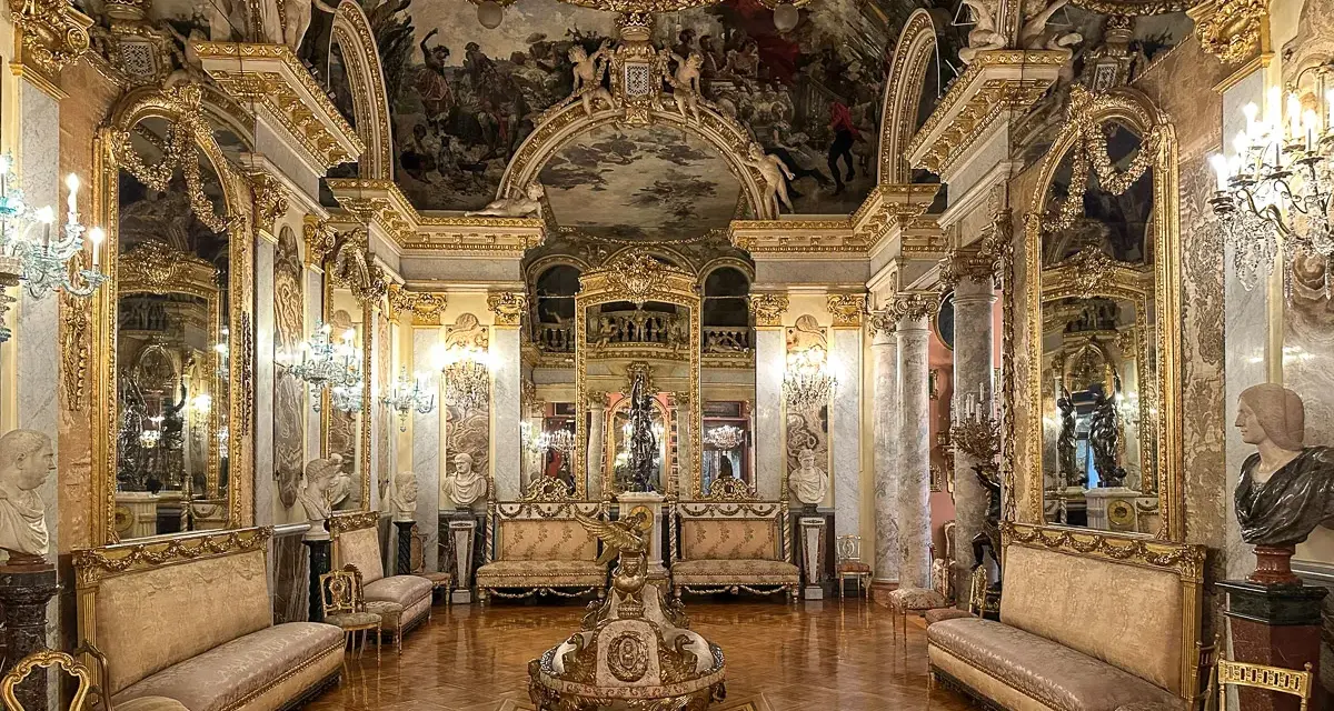 Złocone wnętrze pałacowe, przypominające muzeum w Madrycie, z malowidłami na suficie i bogatymi zdobieniami.