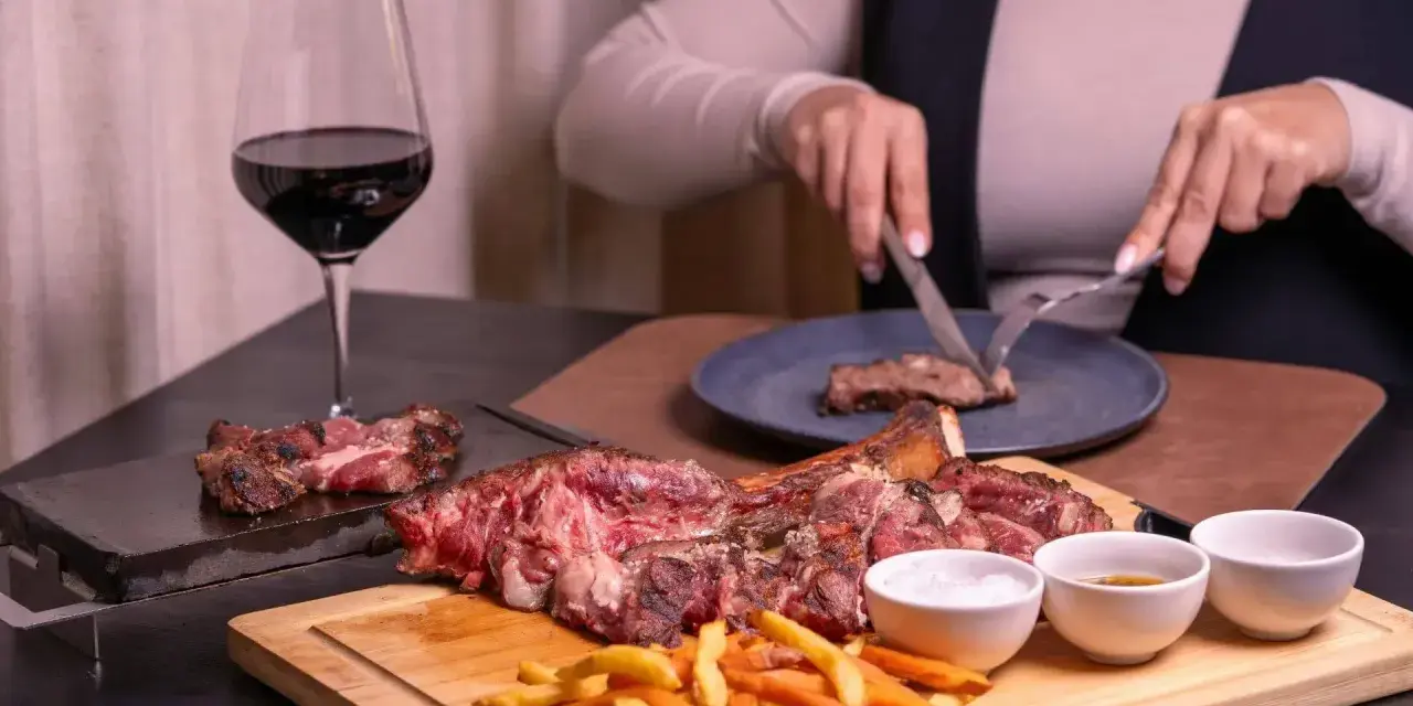 Idealne wino do dziczyzny? Czerwone, pełne, jak to w kieliszku obok soczystego steka i frytek. Ktoś kroi kolejny kawałek.