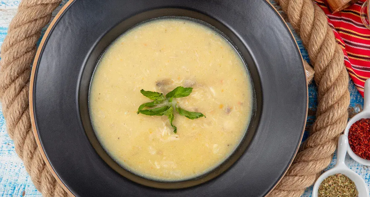 Un plato de sopa de pescado cremoso y caliente, decorado con hojas verdes, sobre un fondo rústico.