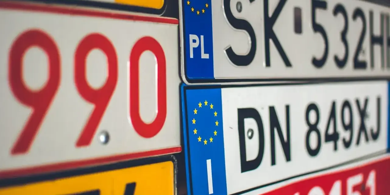 Zbliżenie na stos tablic rejestracyjnych z różnymi kody samochodowe. Widoczne numery to m.in. 990, SK 532HH, DN 849XJ.