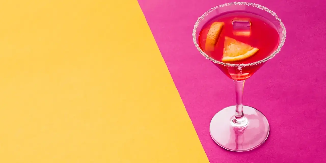 Elegancki cosmopolitan drink co zamiast żurawiny, z pomarańczą i lodem, na tle żółto-różowym.