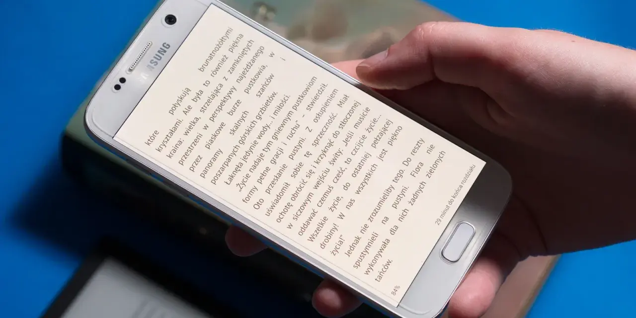 Dłoń trzyma smartfon, na którym wyświetlona jest książka do czytania na telefonie.