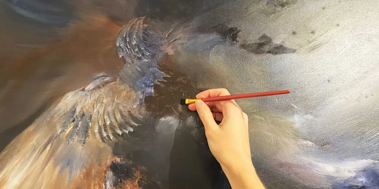 Une main tient un pinceau rouge, ajoutant des touches de lumière à une peinture à l'huile complexe d'un ange. La peinture à l'huile, c'est bien difficile, mais le résultat est saisissant.
