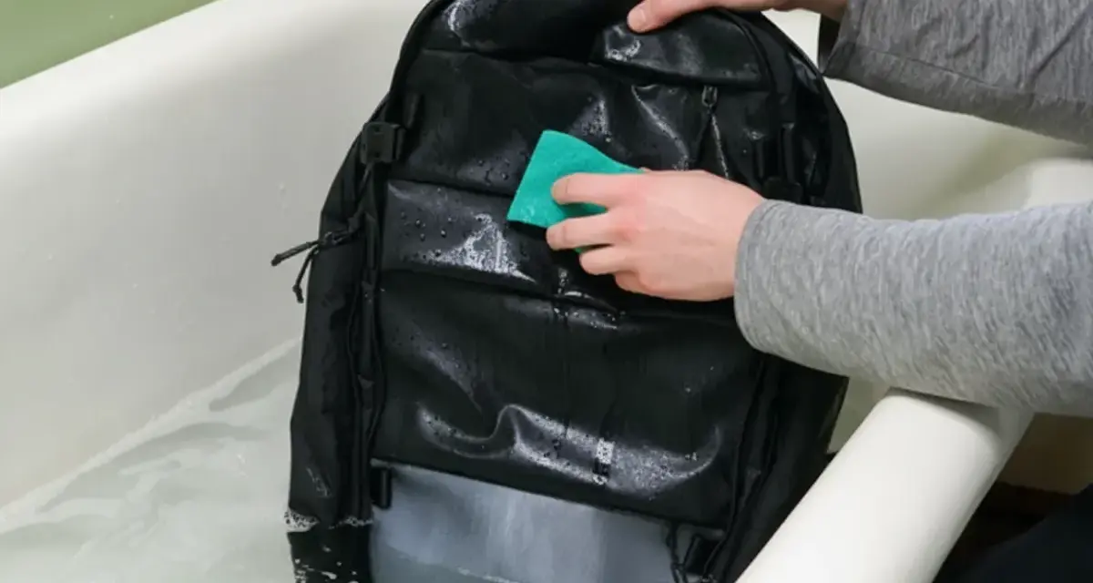 Se puede lavar una mochila en la lavadora. Alguien limpia una mochila negra en una bañera con agua y jabón.