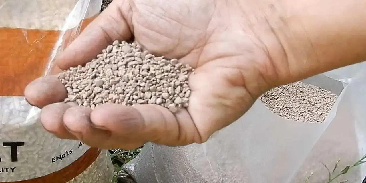 Mano che tiene un pugno di nocciolino pellet, con sacchi pieni sullo sfondo.