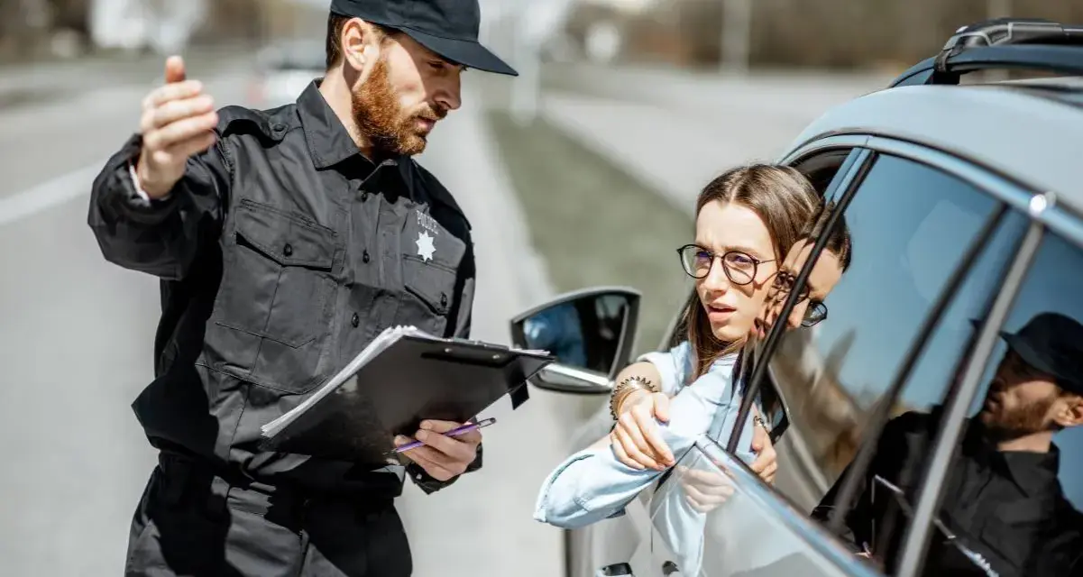 Policjant po 40. zatrzymuje kierowcę do kontroli. Kobieta w okularach wygląda na zaniepokojoną.