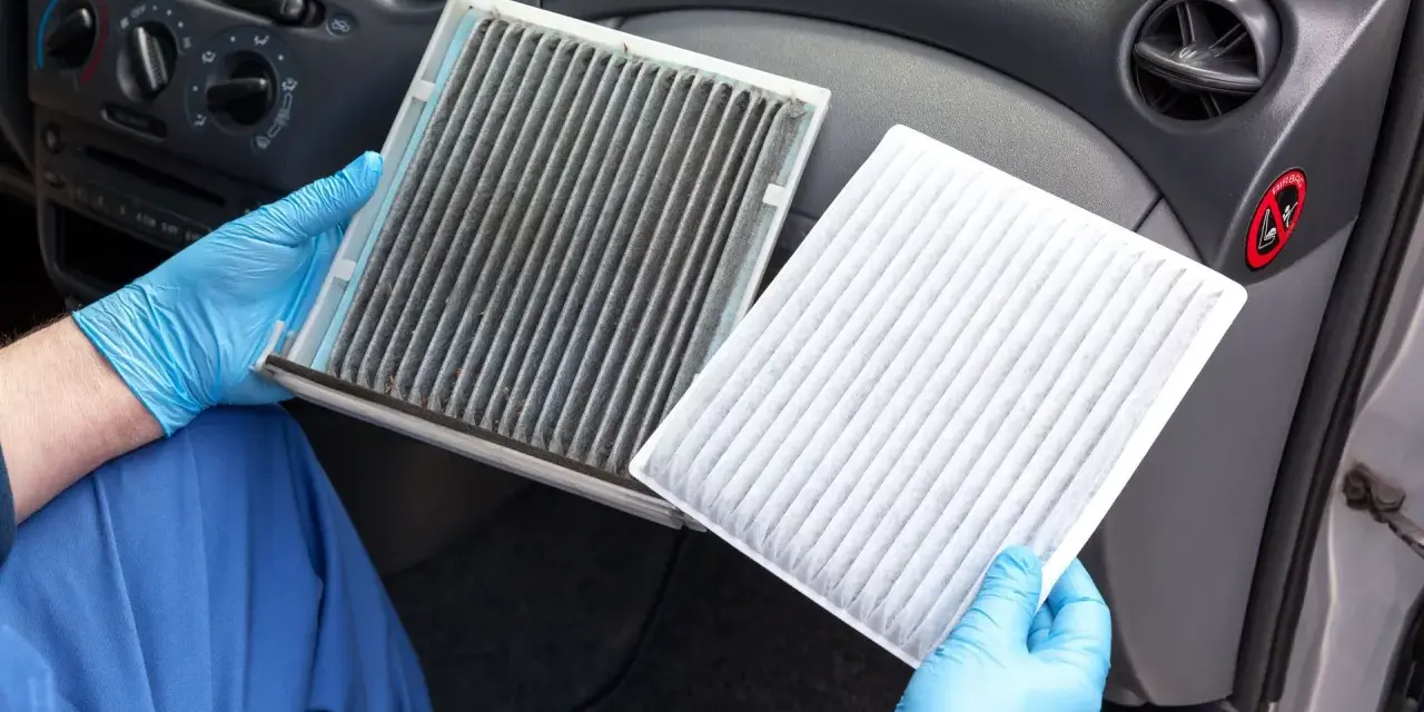 A dirty cabin air filter can make your car smell. A gloved hand holds a very dirty filter next to a clean, white one, showing the stark contrast.