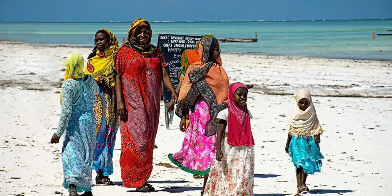 Kobiety w kolorowych strojach spacerują po plaży. Czy Zanzibar to państwo? Tak, to autonomiczny region Tanzanii, znany z pięknych plaż.