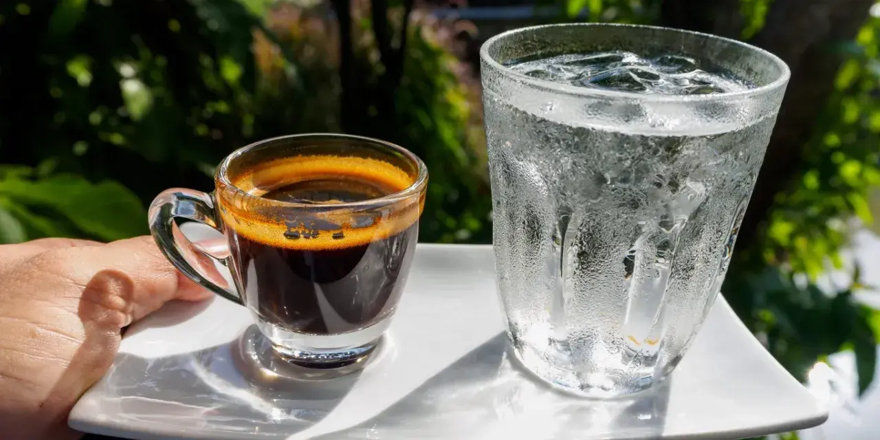 Espresso i szklanka wody z lodem na białym talerzyku. Woda do espresso przed czy po?