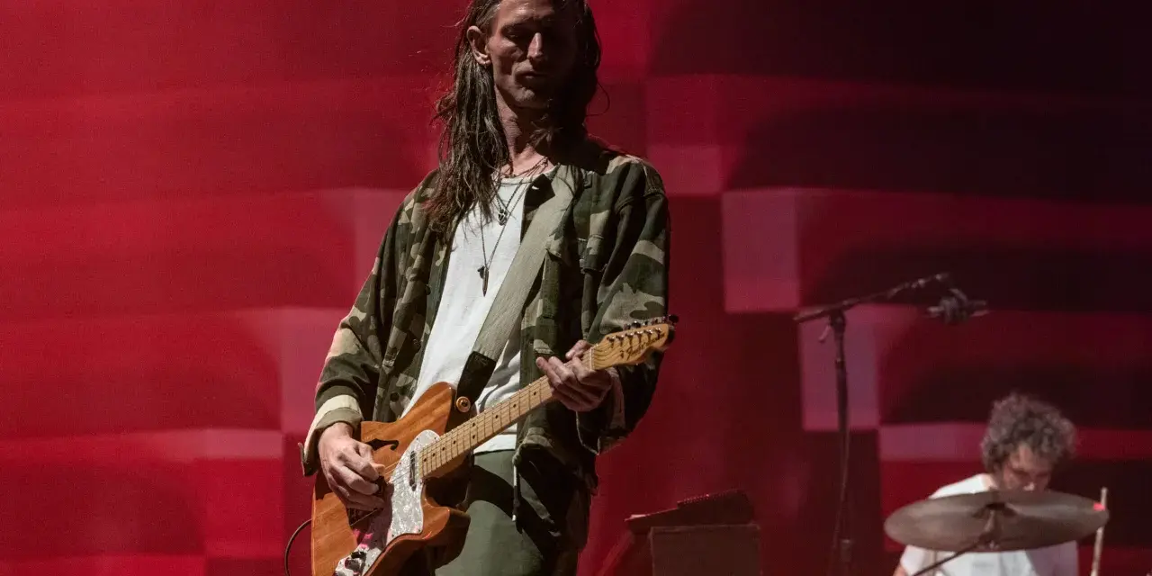Nick Valensi spielt Gitarre auf einer Bühne, im Hintergrund ein Schlagzeuger.