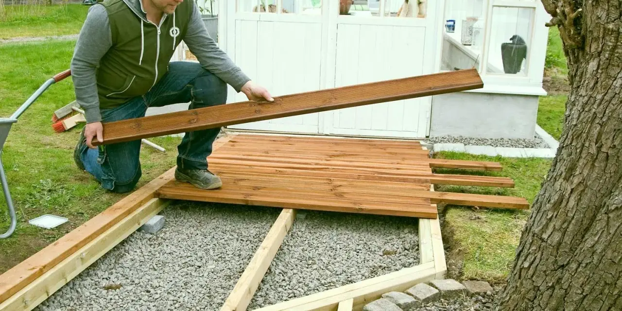 Man bygger trall vid ett växthus. Han håller en träbräda redo att läggas på plats.