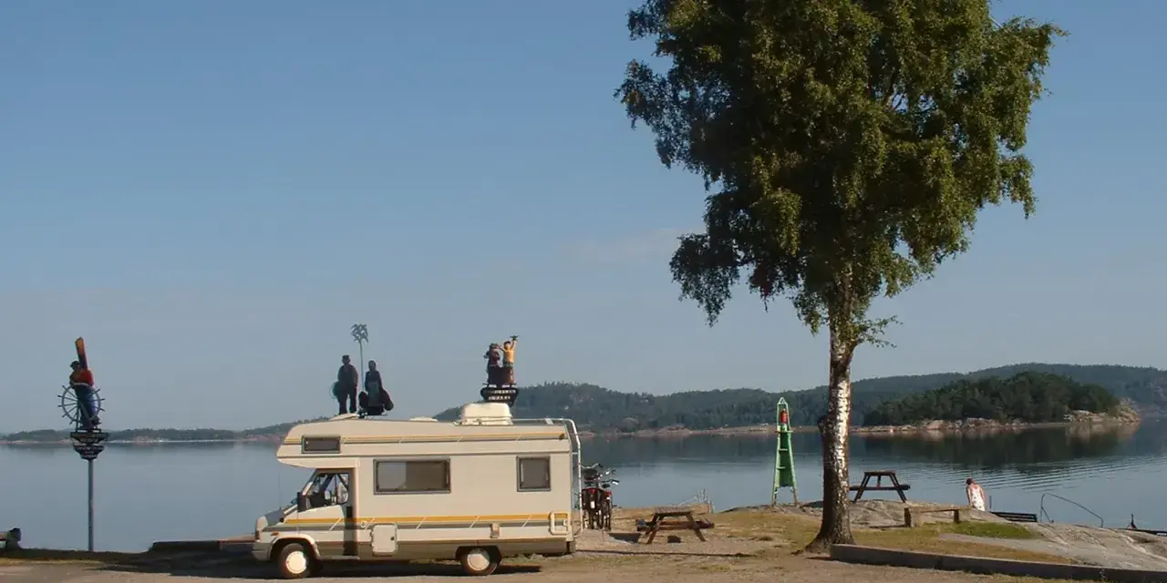 Husbil vid vattnet med figurer på taket, redo för året runt camping. En vacker plats för avkoppling.