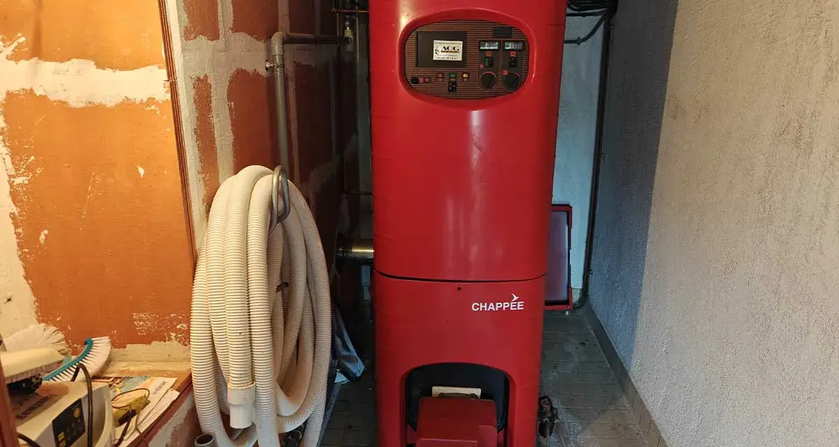 Chaudière rouge Chappée dans une pièce. Un tuyau blanc enroulé est accroché au mur. Pensez à l'assurance chaudière pour votre confort.