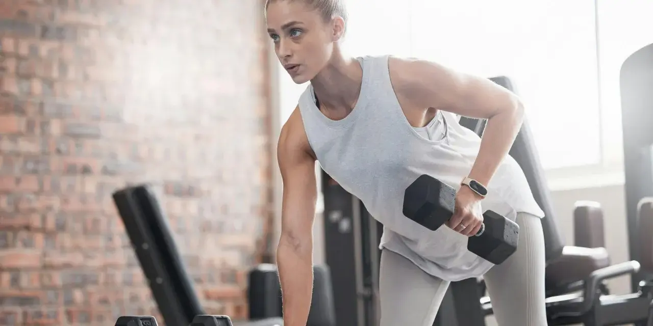 Kvinna tränar med hantlar på gym, fokuserad på att bygga muskler och gå upp i vikt.