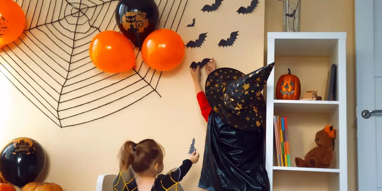 Dzieci tworzą **dekoracje halloween diy**: wieszają nietoperze na ścianie, obok pajęczyny i balonów.