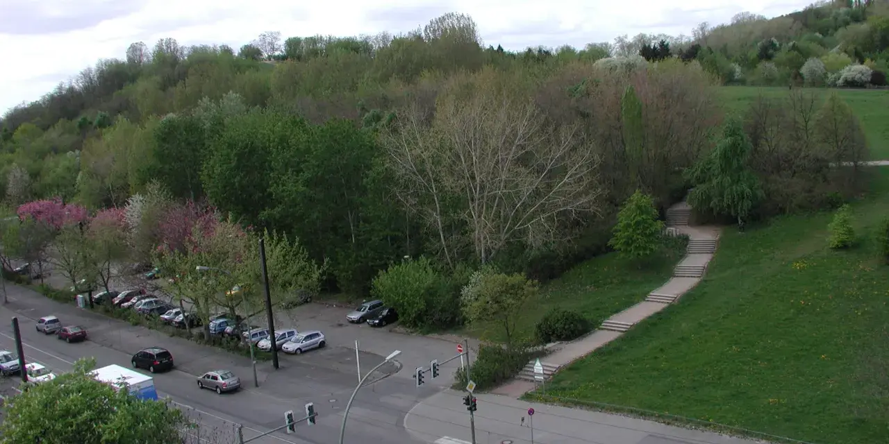 Grüne Hügel und Bäume im Volkspark Prenzlauer Berg. Autos parken am Straßenrand, eine Treppe führt einen Hang hinauf.
