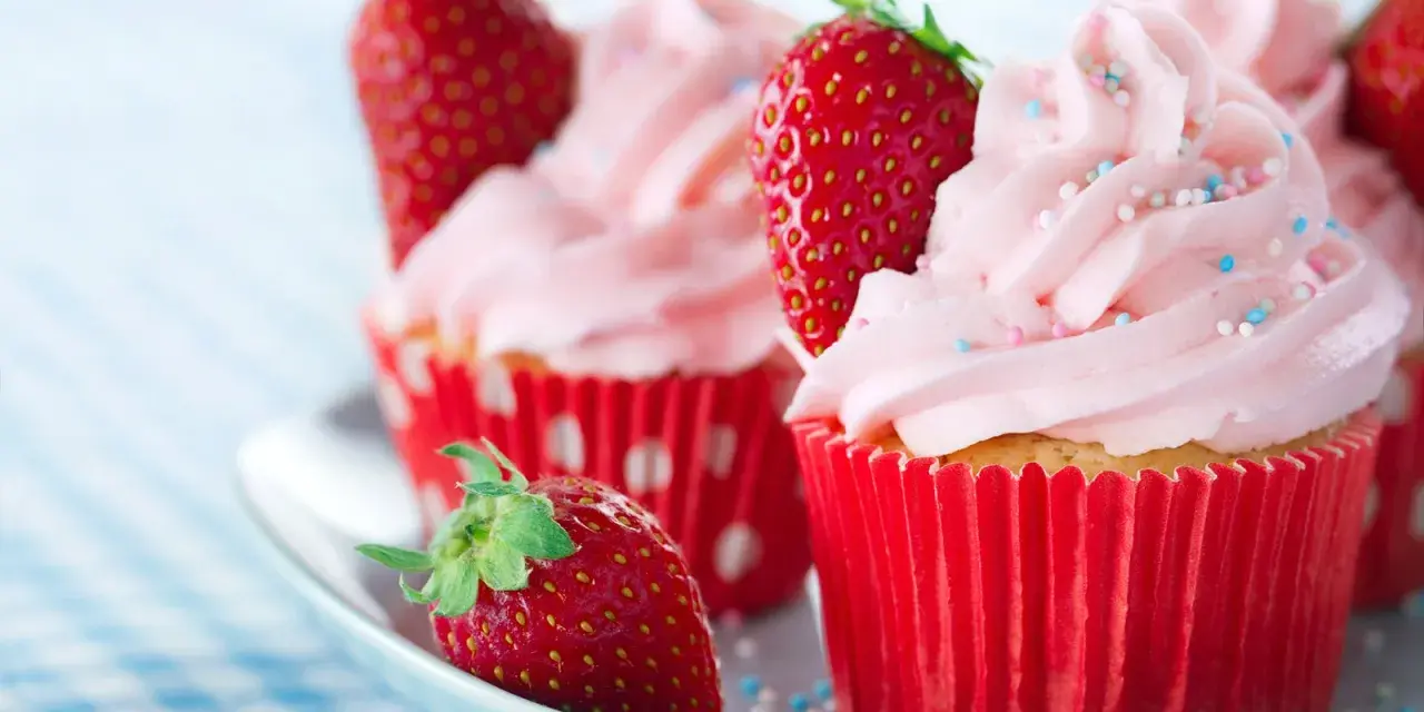 Erdbeer cupcakes mit rosa Zuckerguss und frischen Erdbeeren, verziert mit bunten Streuseln.