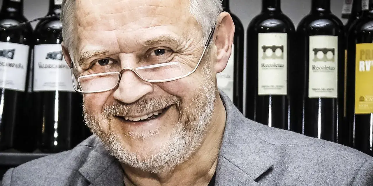 Marek Kondrat, z uśmiechem i okularami, na tle butelek wina. Jego majątek to nie tylko sukcesy zawodowe, ale i pasja do trunków.
