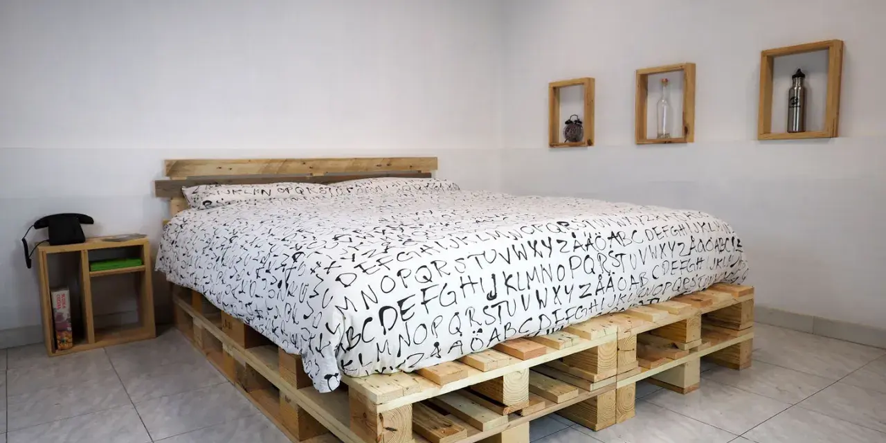 Un letto fai da te economico realizzato con pallet di legno, con un copriletto bianco e nero a tema alfabetico.