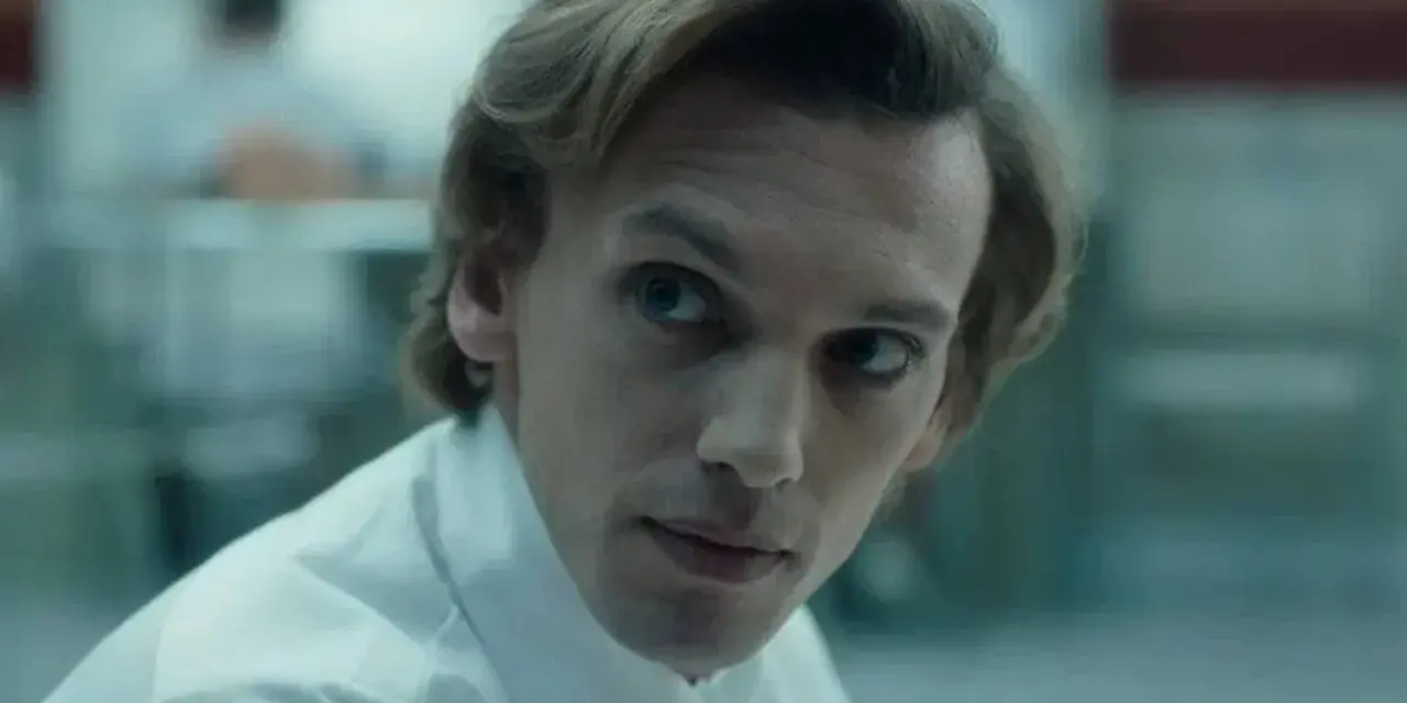 Henry Creel, znany jako Vecna z 001 stranger things, w białej koszuli, patrzy z uwagą.