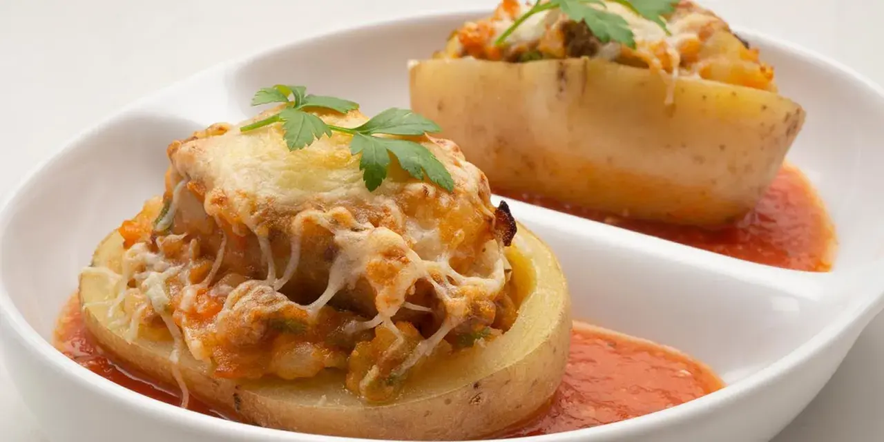 Patatas rellenas de carne de la abuela, gratinadas con queso y perejil, servidas con salsa de tomate.