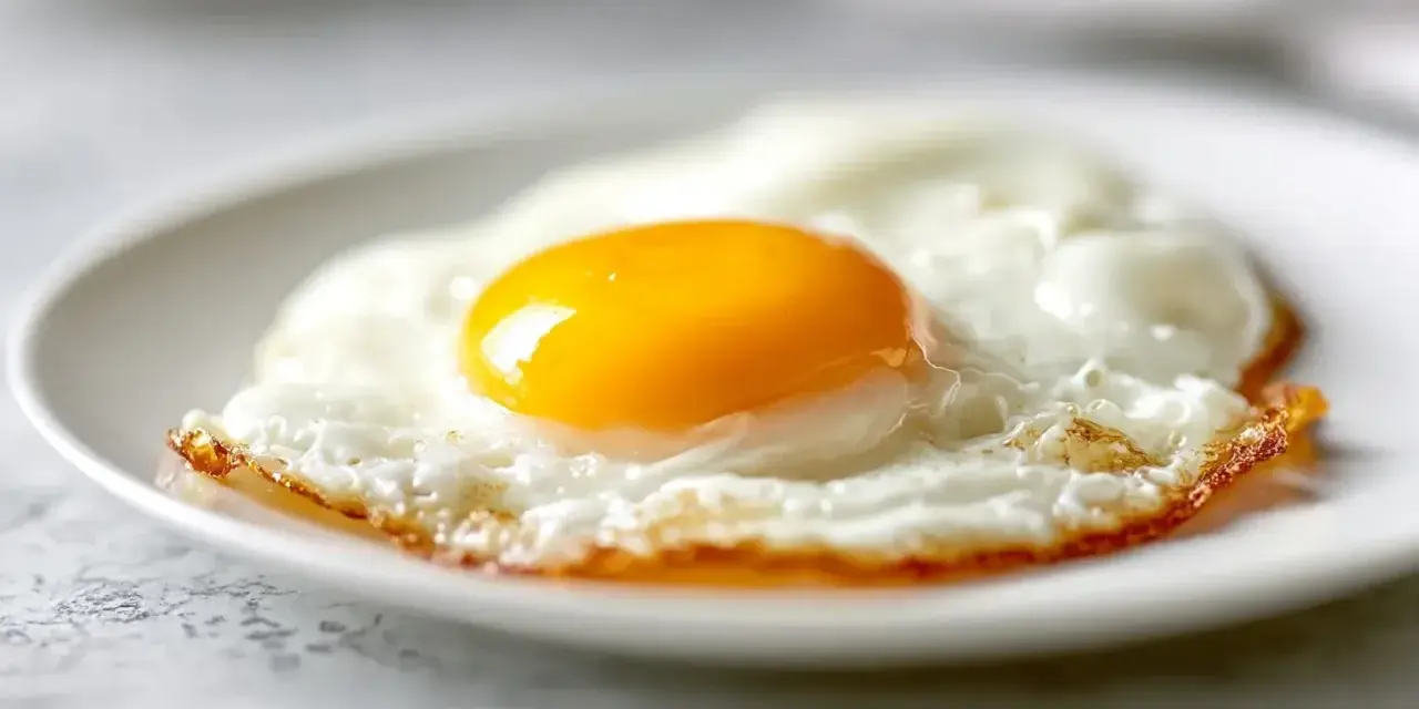Un œuf au plat parfait, cuit à la perfection dans l'air fryer, avec un jaune d'or éclatant sur un lit de blanc d'œuf aérien.