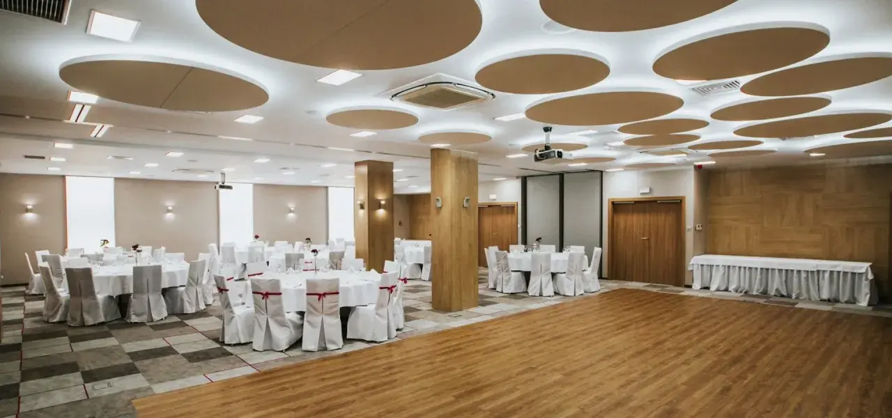 Elegancka sala bankietowa gotowa na wesele we wrześniu. Okrągłe stoły z białymi pokrowcami i czerwonymi wstążkami czekają na gości.